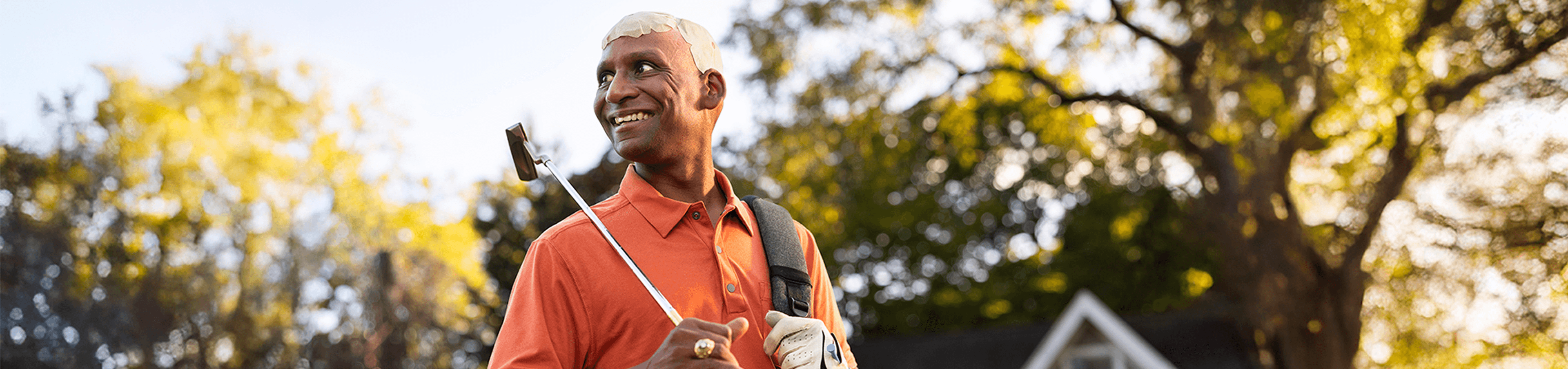Ashok outdoors with a golf club with Optune Gio transducer arrays on his head while carrying the Optune Gio device in the backpack.